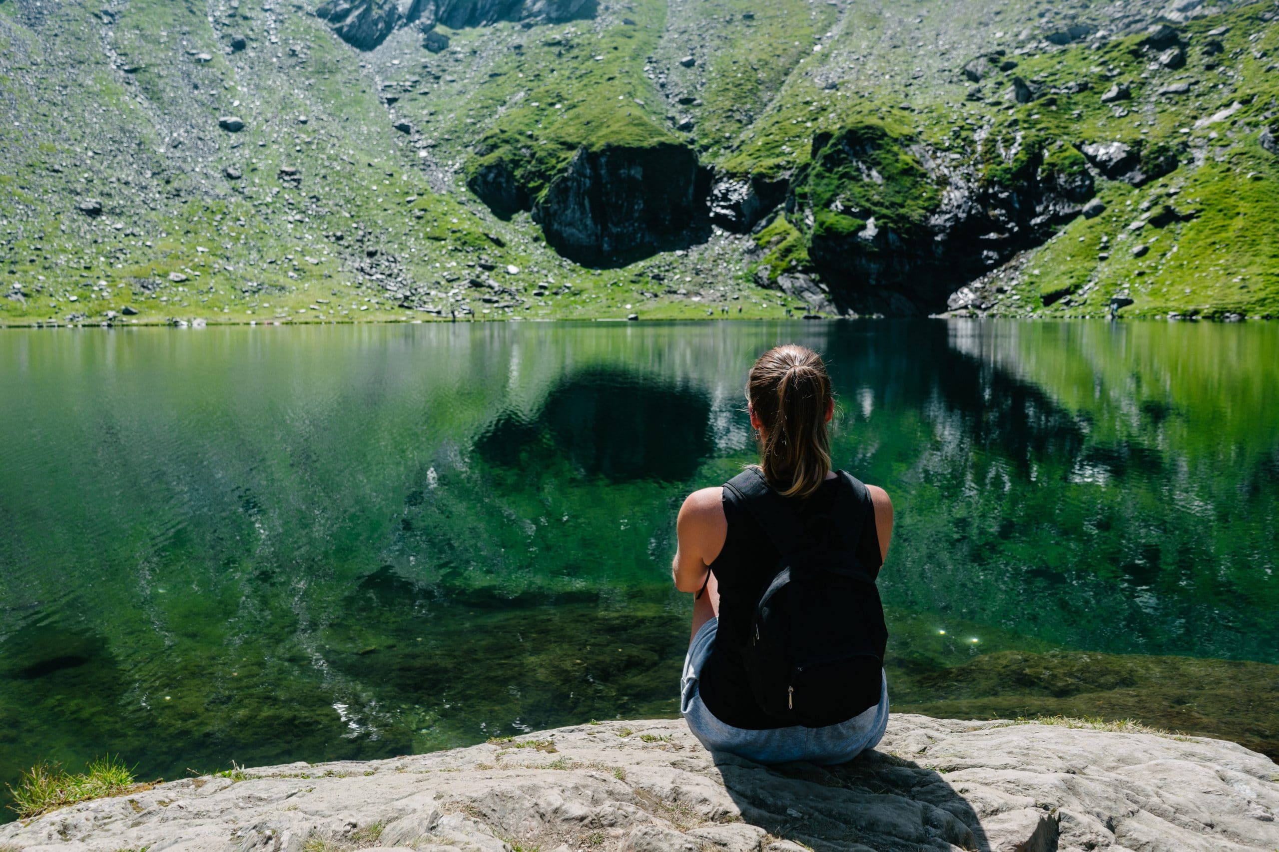 A woman sat on a rock opposite a lake.