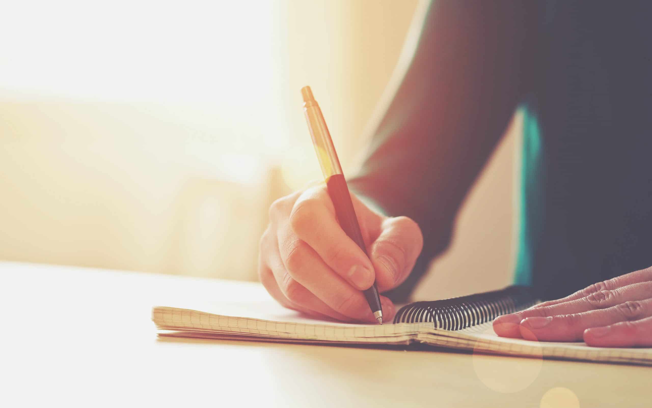 Female hands holding a pen and writing in a notebook.