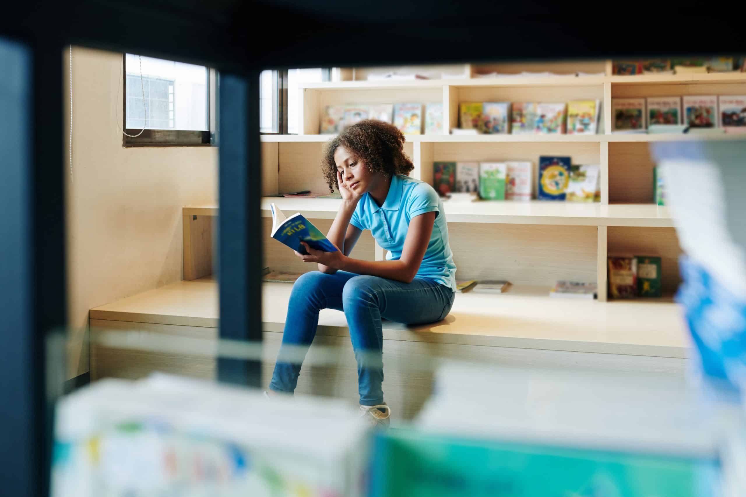 A young girl reading a book in her local library.