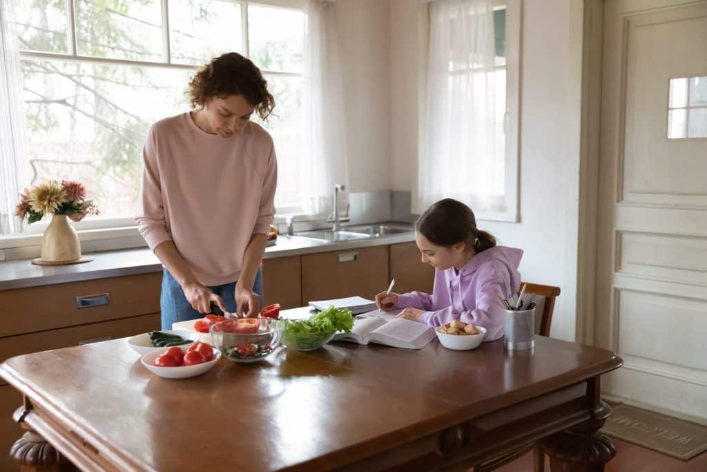 A teenage girl studying whilst her mum prepares a healthy meal.