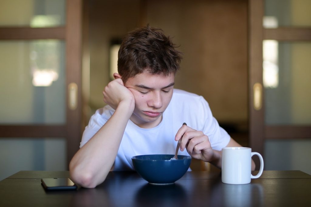 A tired teenage boy eating breakfast.