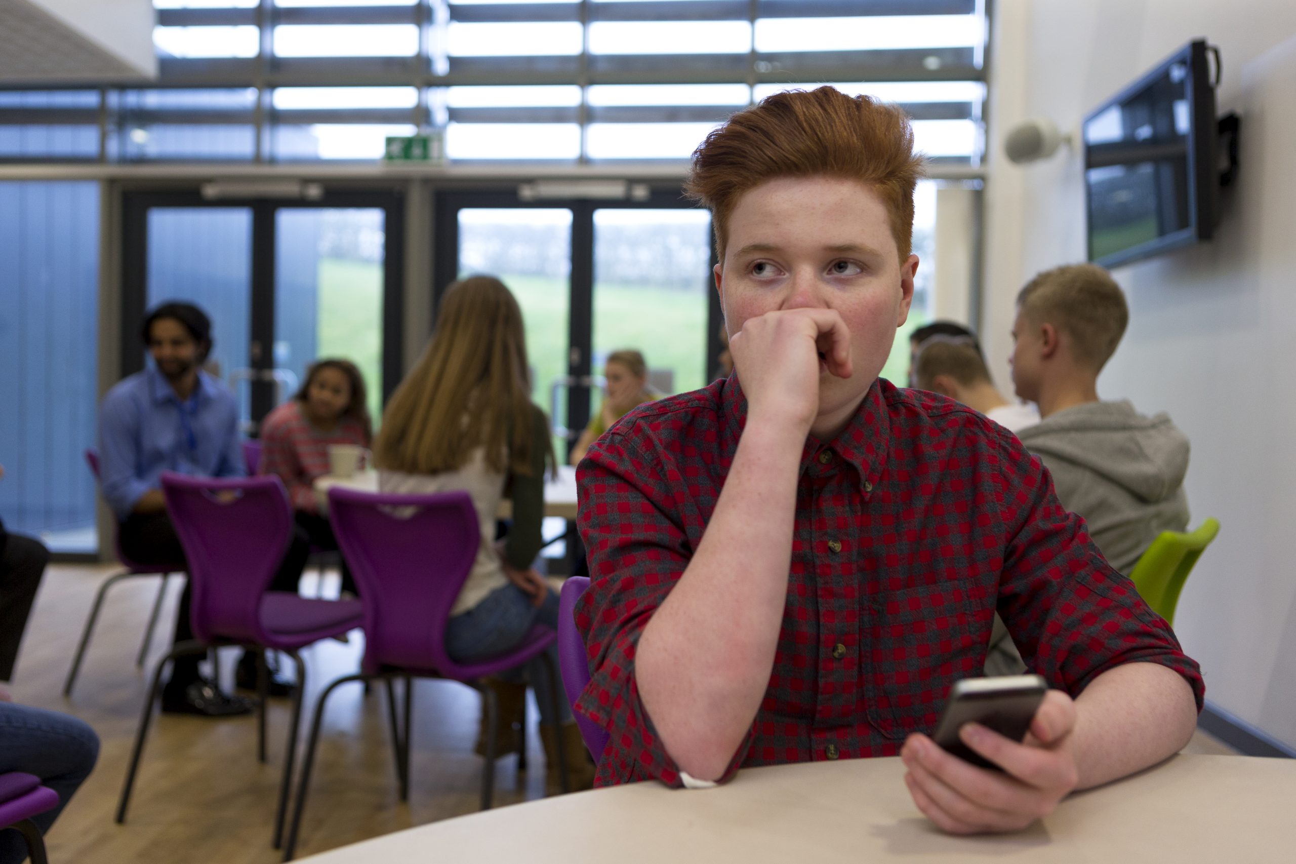 A stressed teenage boy with a smartphone in hand.
