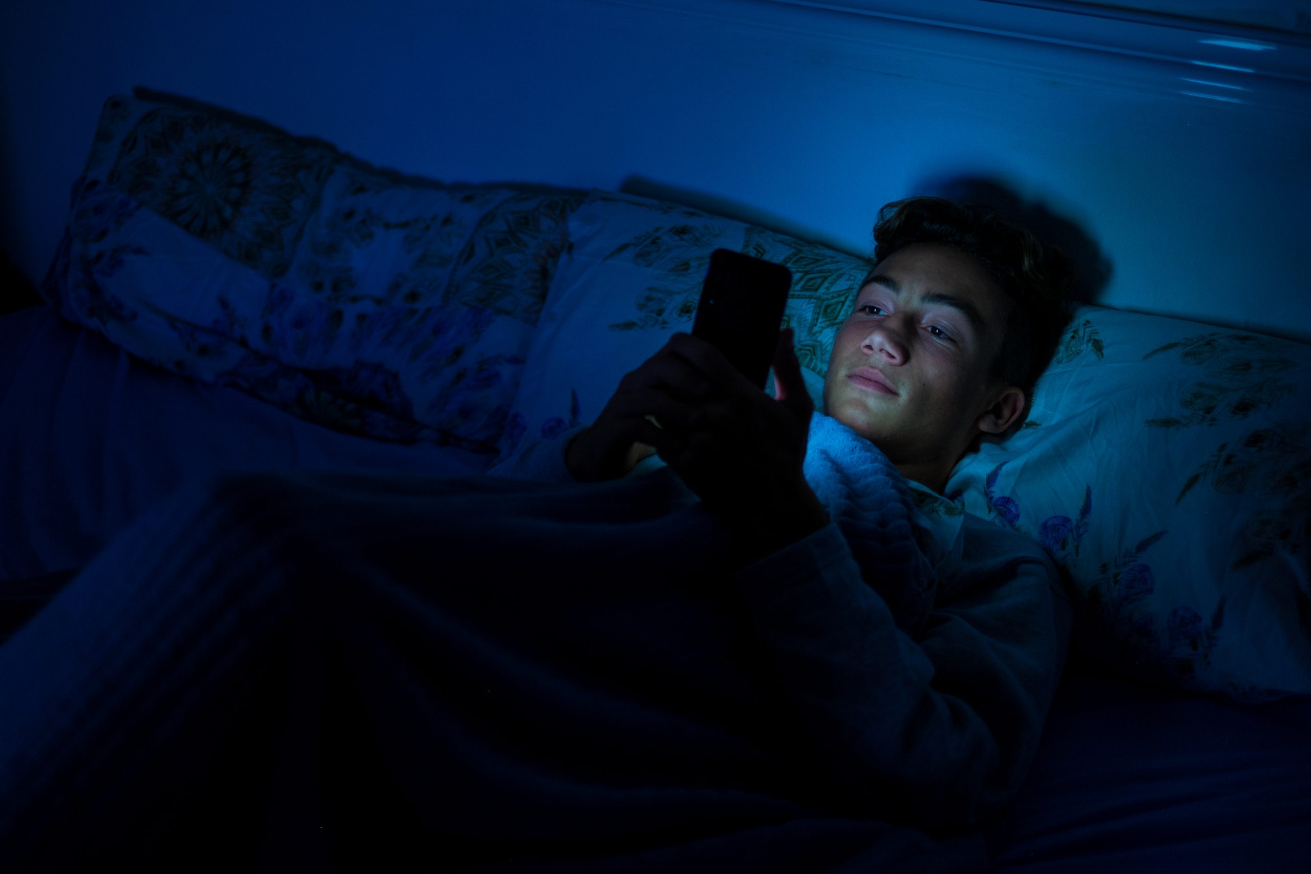 A teenage boy using his phone in bed before going to sleep.