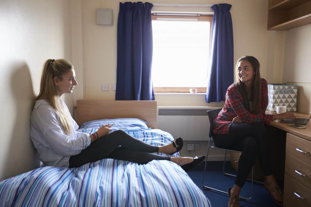 Two female students chatting in a halls of residence bedroom.