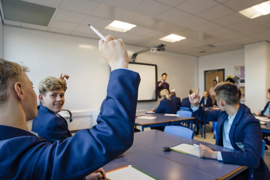 Students putting their hands up to answer a question in class.